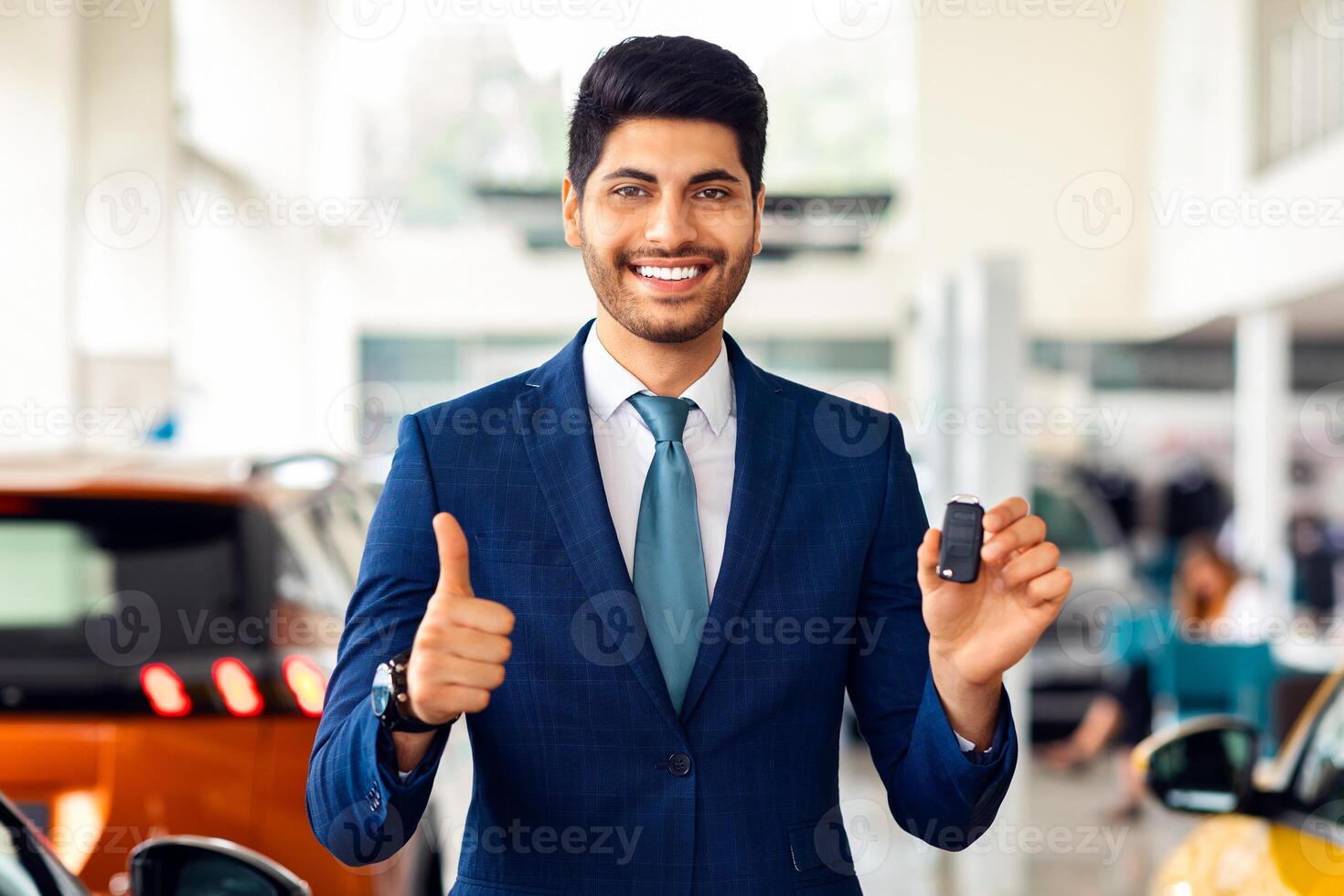 Smiling handsome arabic businessman showing key from his brand new auto and thumb up, copy space. Rich middle-eastern man in stylish suit buying automobile, recommending luxury dealership car salon photo