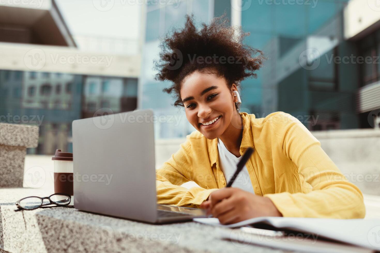 E-Learning. Happy African American Student Girl At Laptop Smiling To Camera While Taking Notes Learning Online Sitting Outdoors Near University Building. Modern Remote Education photo