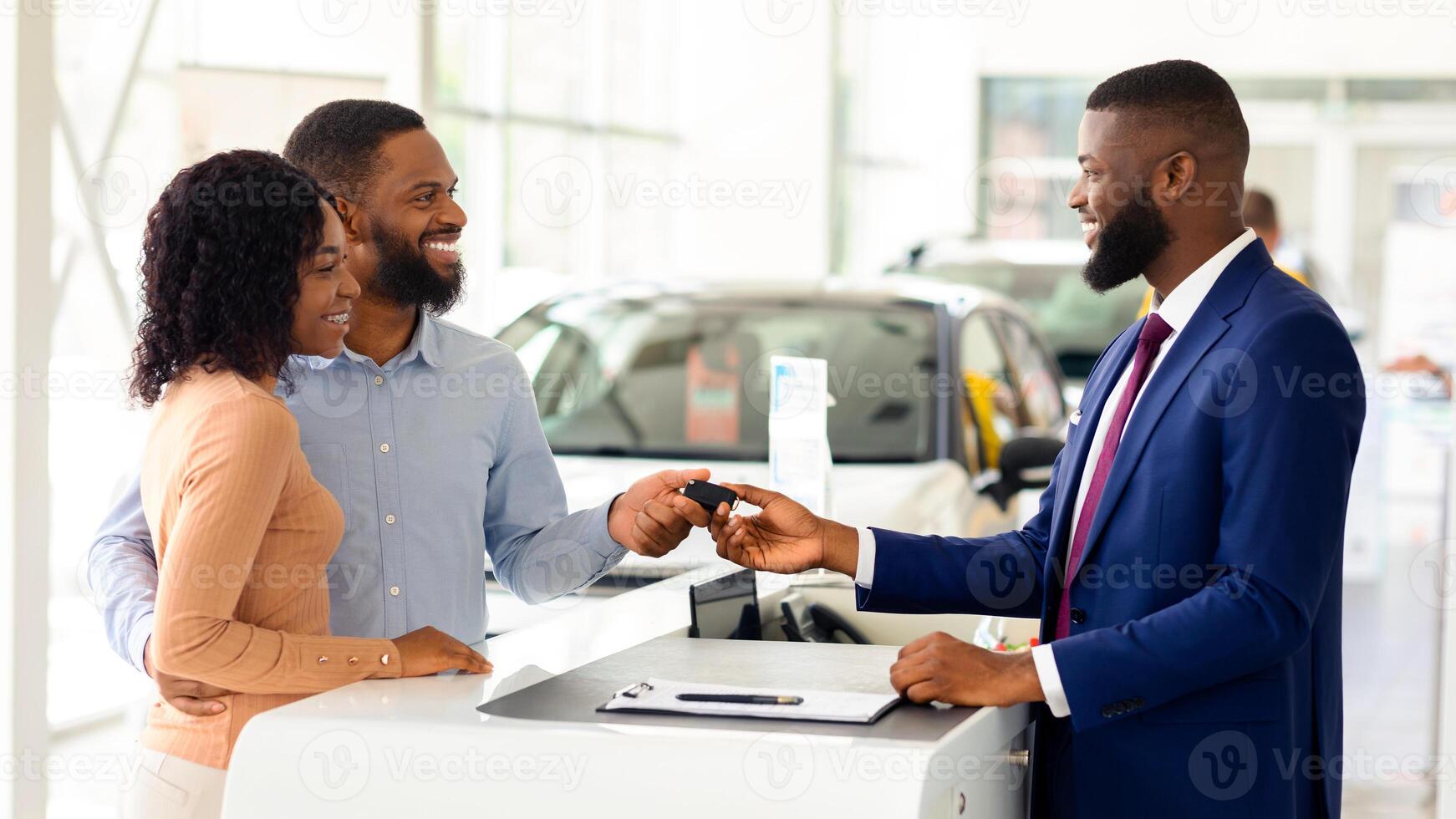 Car Sales. Handsome Black Manager Giving Key To Happy Couple In Dealership Center After Buying New Vehicle, Greeting African American Spouses With Successful Purchase In Automobile Showroom photo