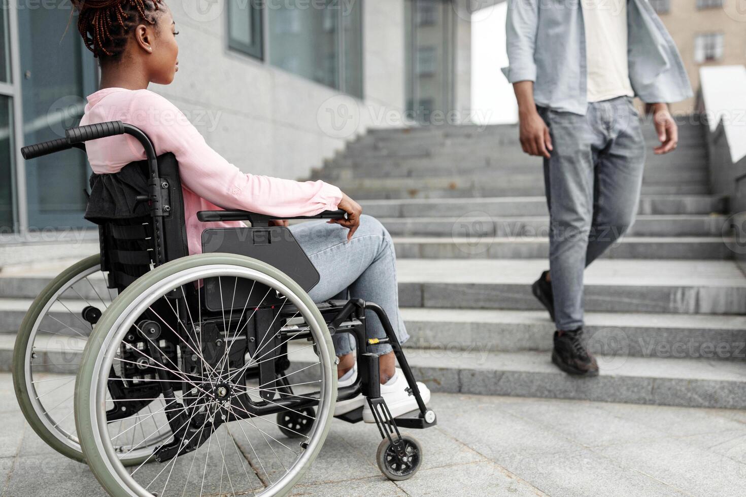 Young black disabled woman suffering from lack of wheelchair friendly facilities, looking at man going down stairs, cannot get home without ramp. Handicapped people problems concept photo