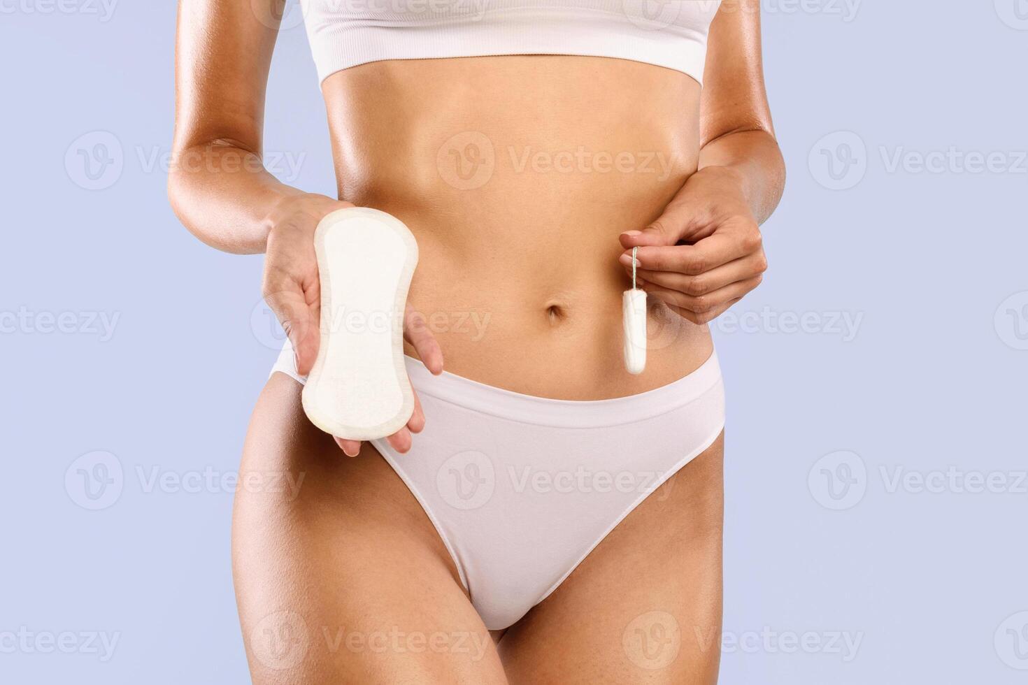 Feminine Hygiene Products Choice And Alternative. Closeup cropped view of unrecognizable lady holding absorbent tampon and sanitary napkin near belly standing isolated on blue studio background photo