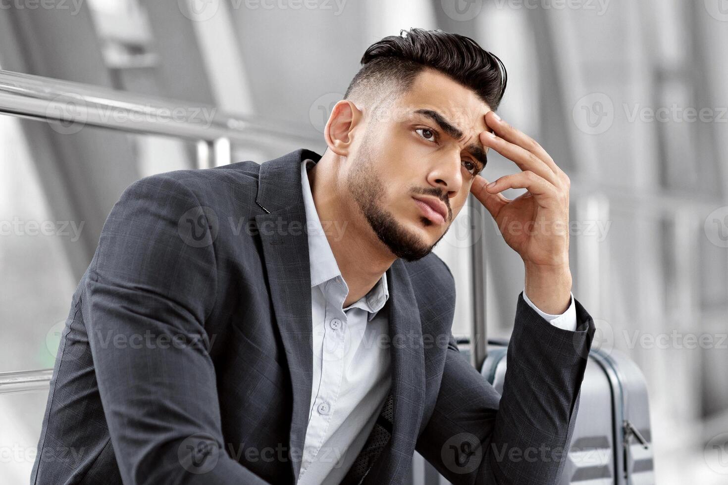 Flight Delay. Portrait Of Pensive Arab Man Waiting With Luggage In Airport , Thoughtful Young Middle Eastern Guy Sitting Next To Suitcase At Terminal Corridor, Tired Of Long Trip, Copy Space photo