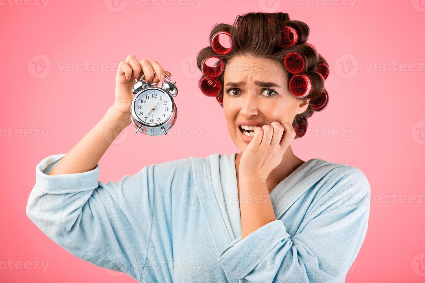 Stressed Housewife Holding Clock Being Late With Housework Chores Standing On Yellow Background. Studio Shot photo