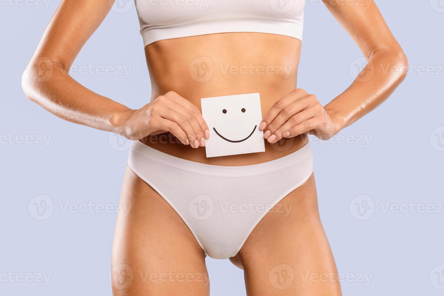 Female Health. Healthy Woman With Beautiful Fit Slim Body Holding White Paper Card With Happy Smiley Emoji Face In Hands Near Belly, Closeup Cropped, Blue Studio Background. Good Digestion Concept photo