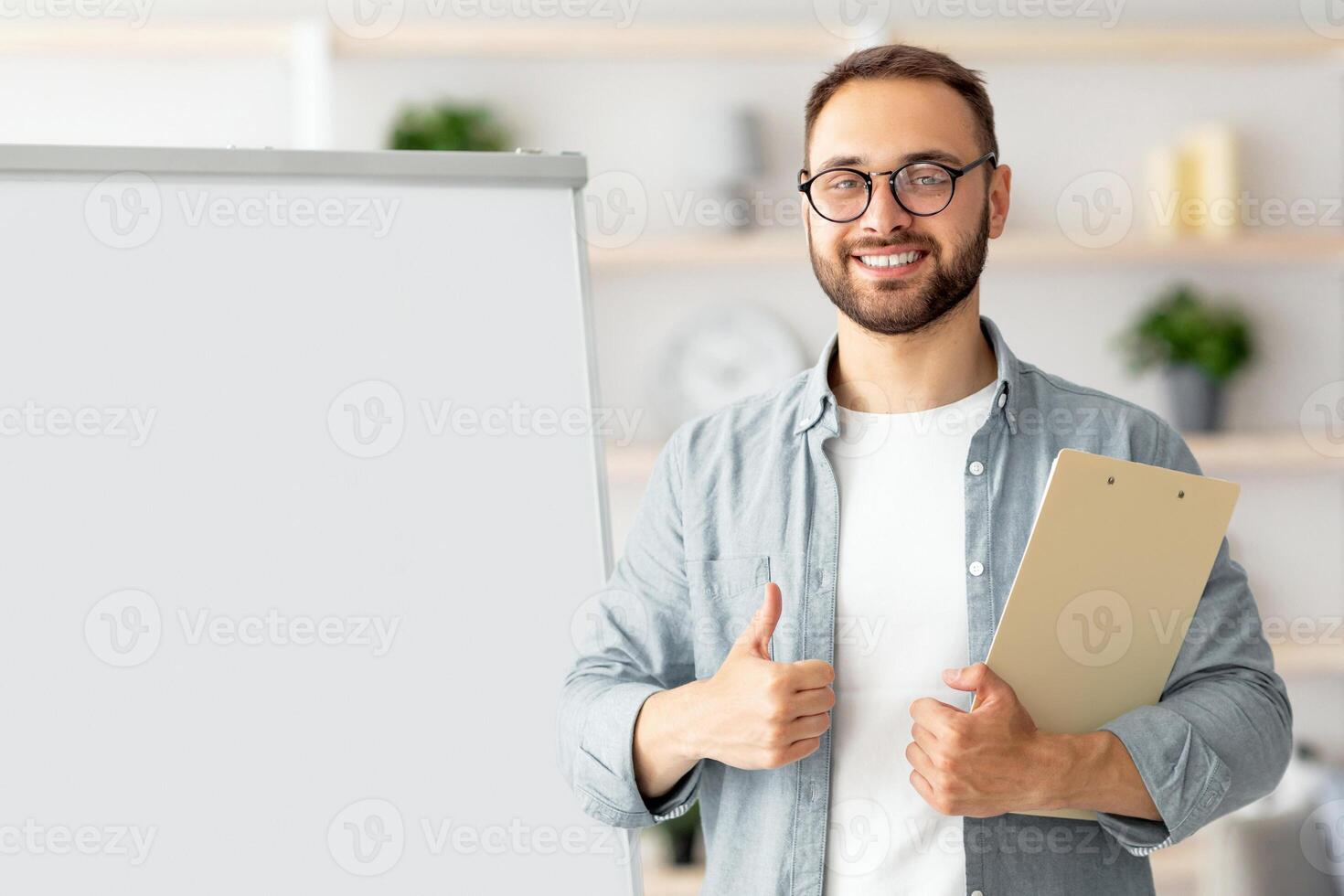 Positive male teacher showing thumb up gesture near blackboard, recommending new online foreign languages school, teaching English on internet. Remote education during covid concept photo
