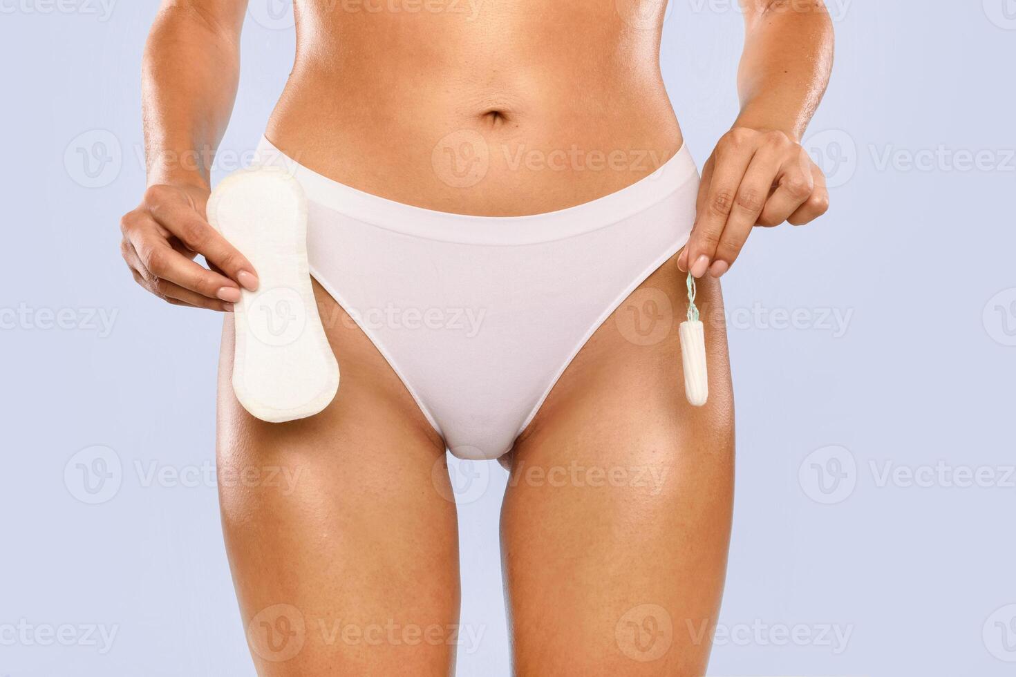 Female Period and Intimate Hygiene. Closeup cropped view of young woman in white panties holding tampon vs clean menstrual pad near hips standing isolated on blue studio background, banner photo