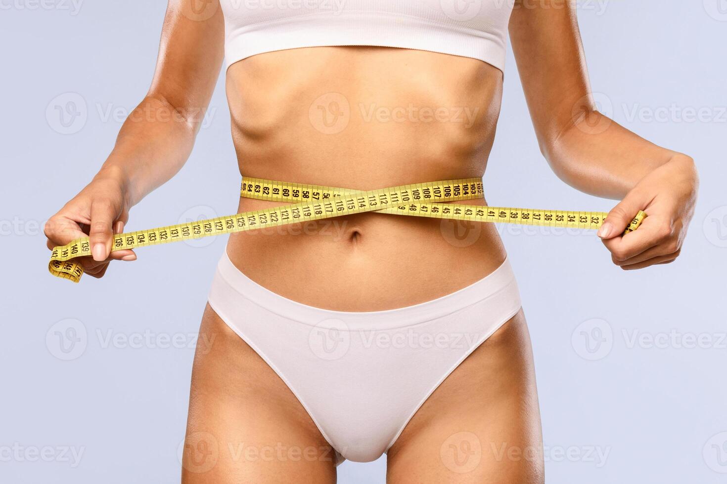 Successful Weightloss And Dieting. Closeup Of Slim Unrecognizable Lady Measuring Waist With Tape, Happy About Her Body Parameters, Standing Isolated On Blue Studio Background. Slimming Concept. Banner photo