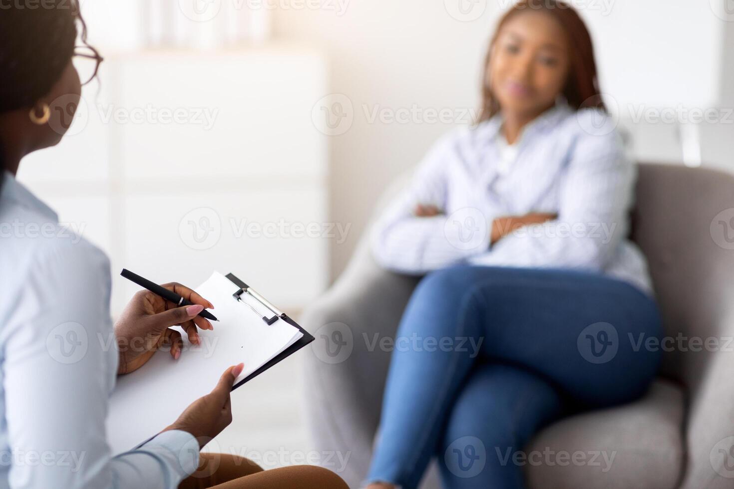 Young black lady receiving professional psychological help at office, selective focus. African American psychotherapist having session with millennial woman. Treatment of ptsd or emotional trauma photo