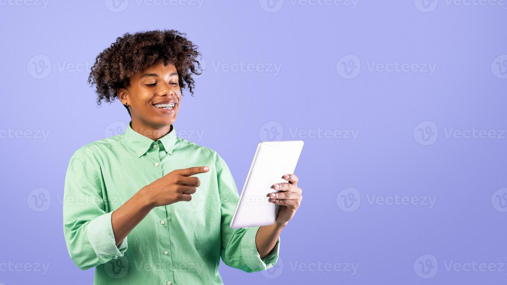 App for students. Happy black teen guy browsing web on tablet pc over blue background and smiling. Excited teenager using touch pad, websurfing online photo