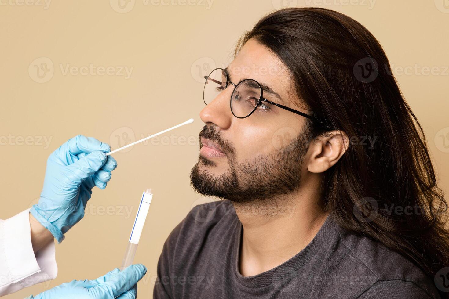 Coronavirus, COVID-19 pcr test concept. Nurse taking nasal swab for coronavirus sample test from potentially infected middle-eastern guy, beige studio background, closeup, copy space photo