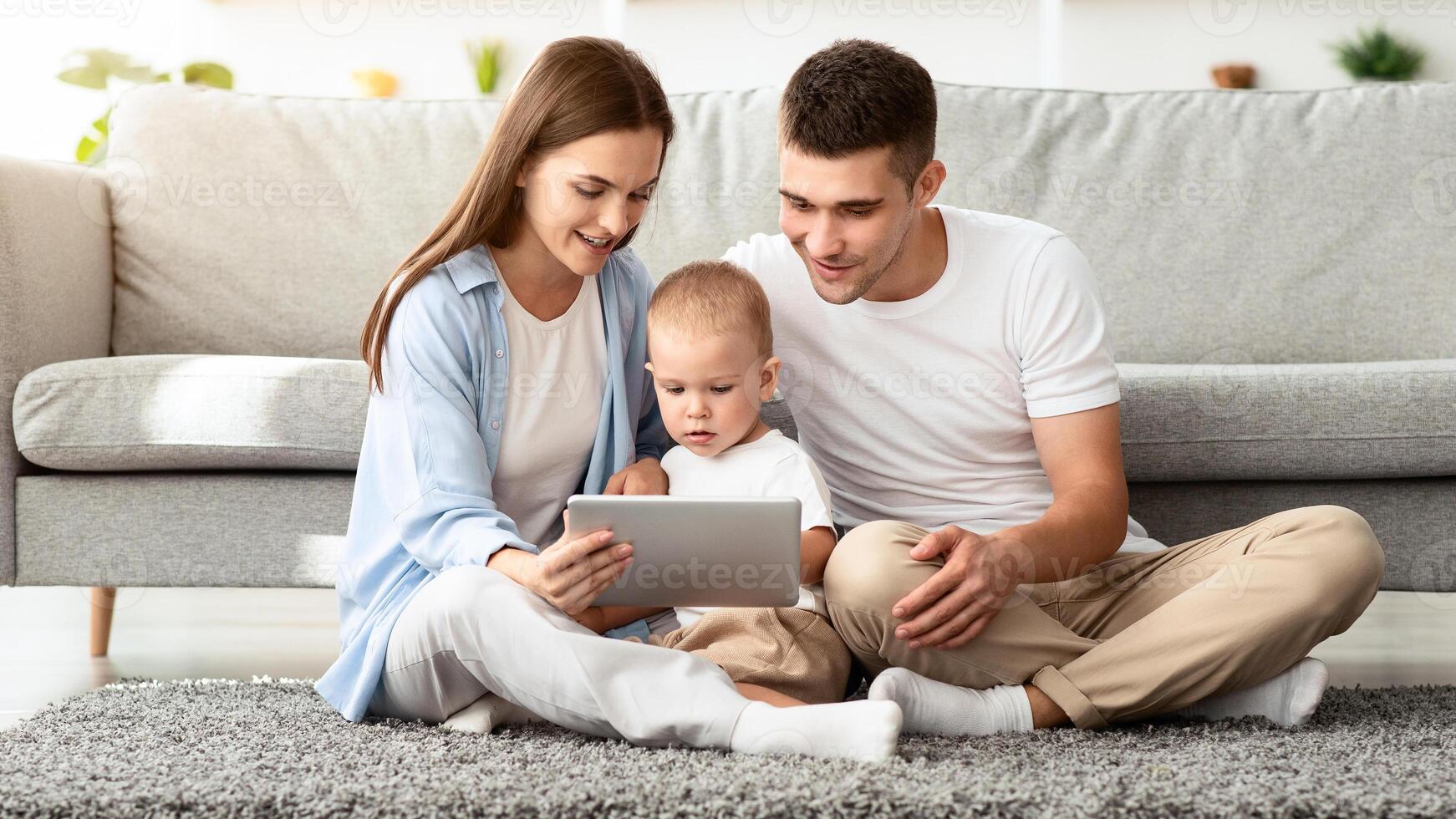 Family Leisure. Millennial Mom And Dad With Their Cute Toddler Son Using Digital Tablet Together At Home, Happy Young Parents Using Modern Gadget While Relaxing With Infant Child In Living Room photo