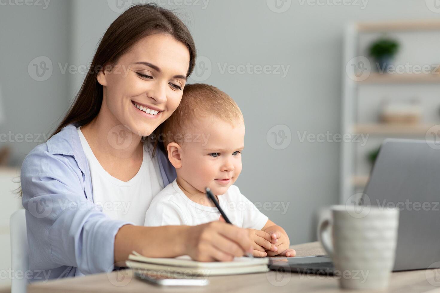 Online Education. Young Woman Holding Baby And Study With Laptop At Home, Cheerful Millennial Lady Taking Notes To Notepad While Watching Webinar On Computer, Enjoying Distance Learning And Maternity photo