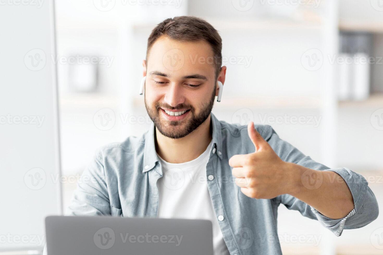 Happy male teacher giving English lesson on web using laptop, gesturing thumb up, recommending foreign languages school. Millennial tutor lecturing over internet from home during covid lockdown photo