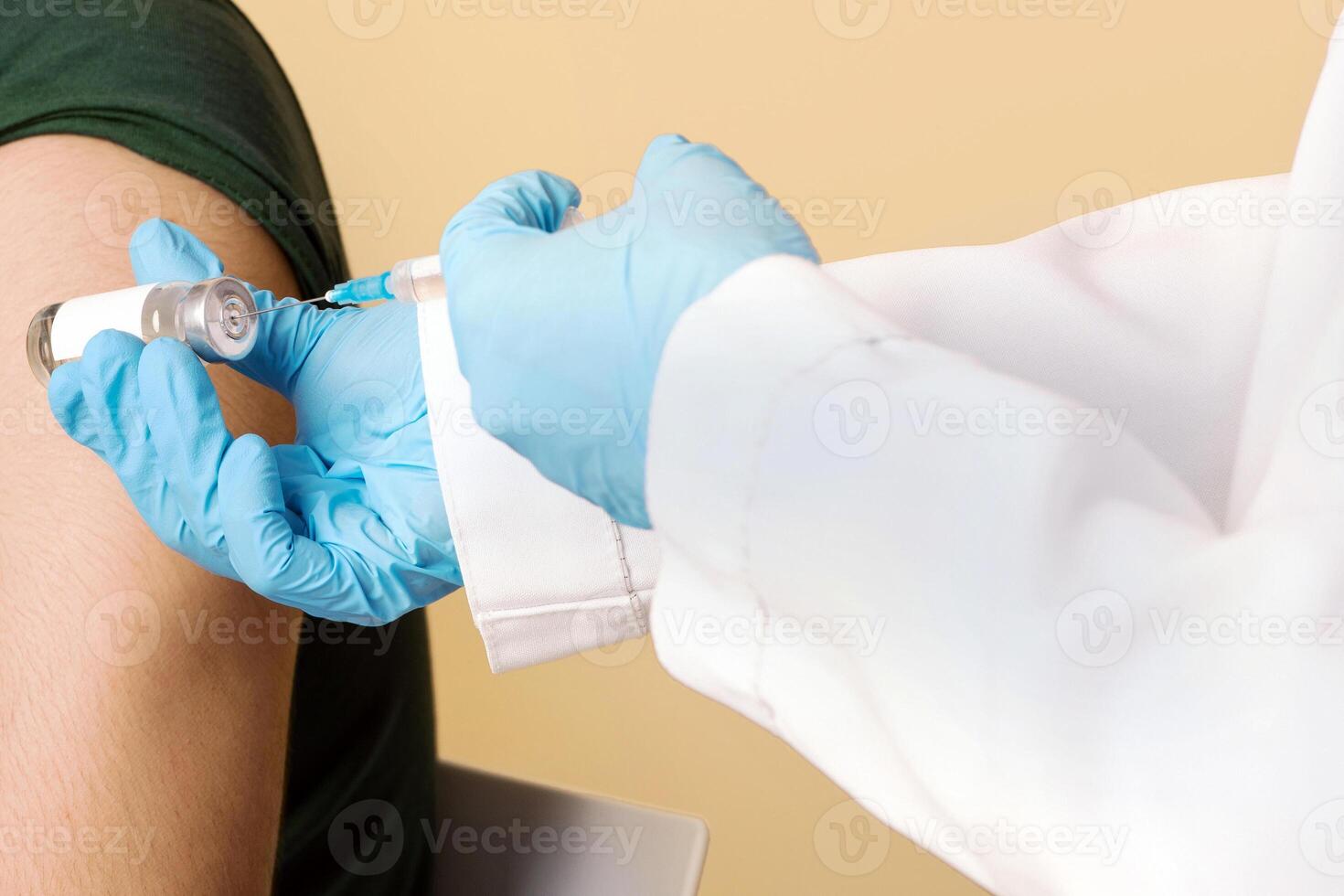 Closeup of nurse hands in medical gloves holding vaccine and syringe, doctor making vaccination against COVID-19 for middle-eastern millennial guy wearing protective mask, beige studio background photo