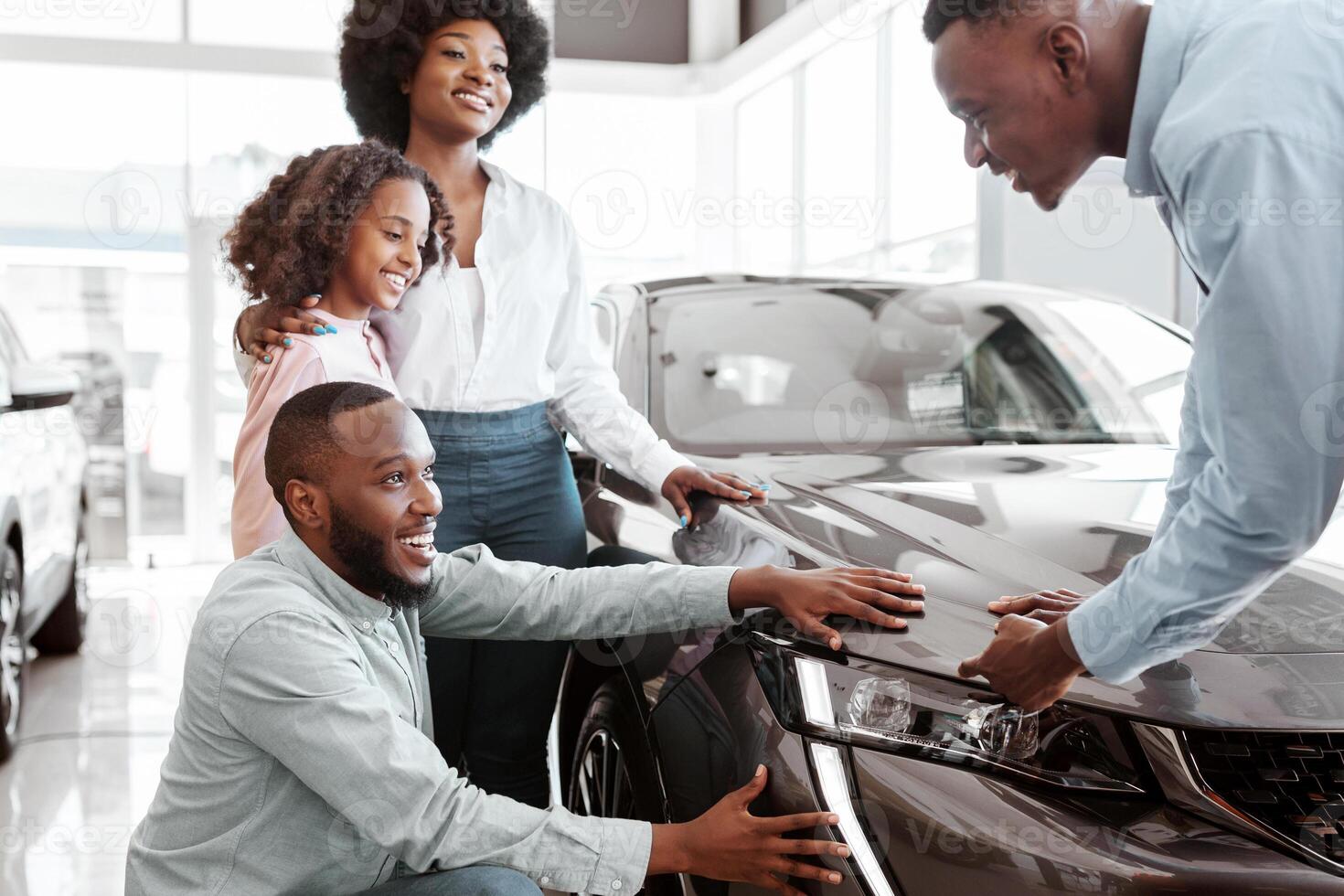 Car sales business. Young black family with cute child selecting vehicle, looking at luxury automobile at showroom. Seller talking to Afro clients, showing them new auto at dealership shop photo