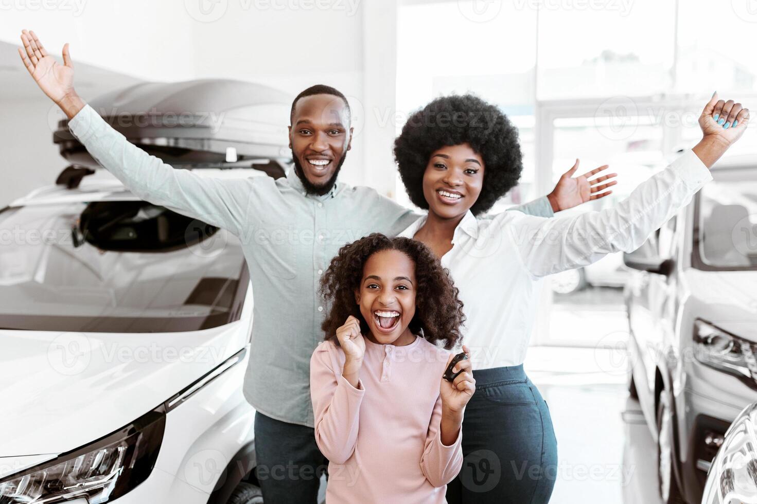 Visiting car dealership. Excited Afro family showing key, shouting WOW, feeling overjoyed about buying new auto, looking at camera, raising hands up at automobile showroom photo