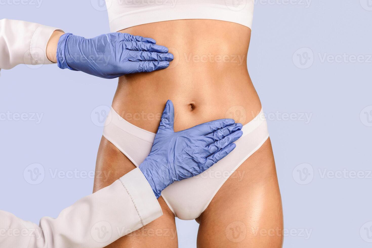 Lipolysis, Making Perfect Body. Young woman getting consultation at plastic surgery clinic, closeup cropped view of abdomen and doctor's hands in protective gloves touching and examining belly fat photo