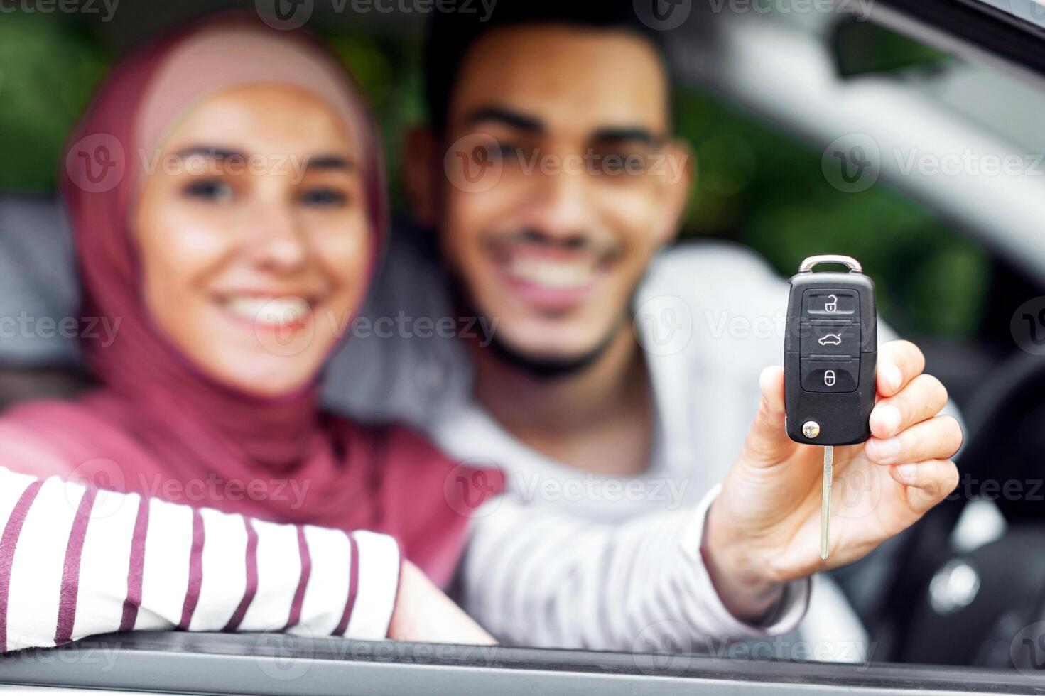 Dreams come true. Glad happy young arab husband and wife in hijab customers show keys at new car, close up. Loan and auto purchase, facial expression and positive emotions from buying own transport photo