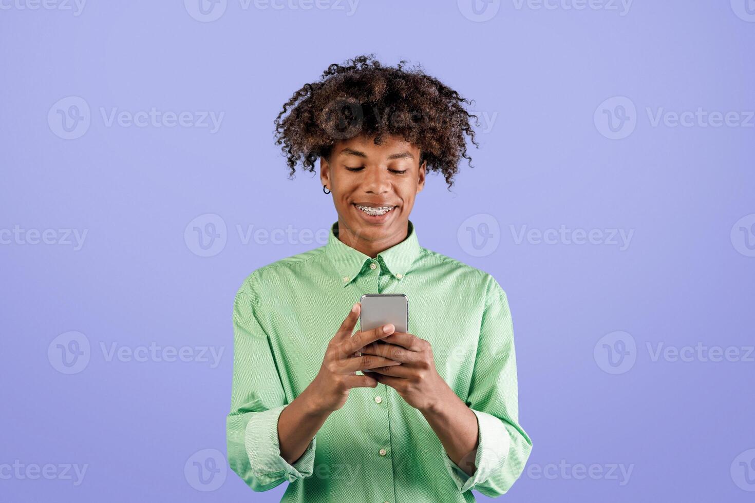 Cool app. Happy african american guy using smartphone, browsing new application or messaging with friends online, standing over blue studio background, copy space photo