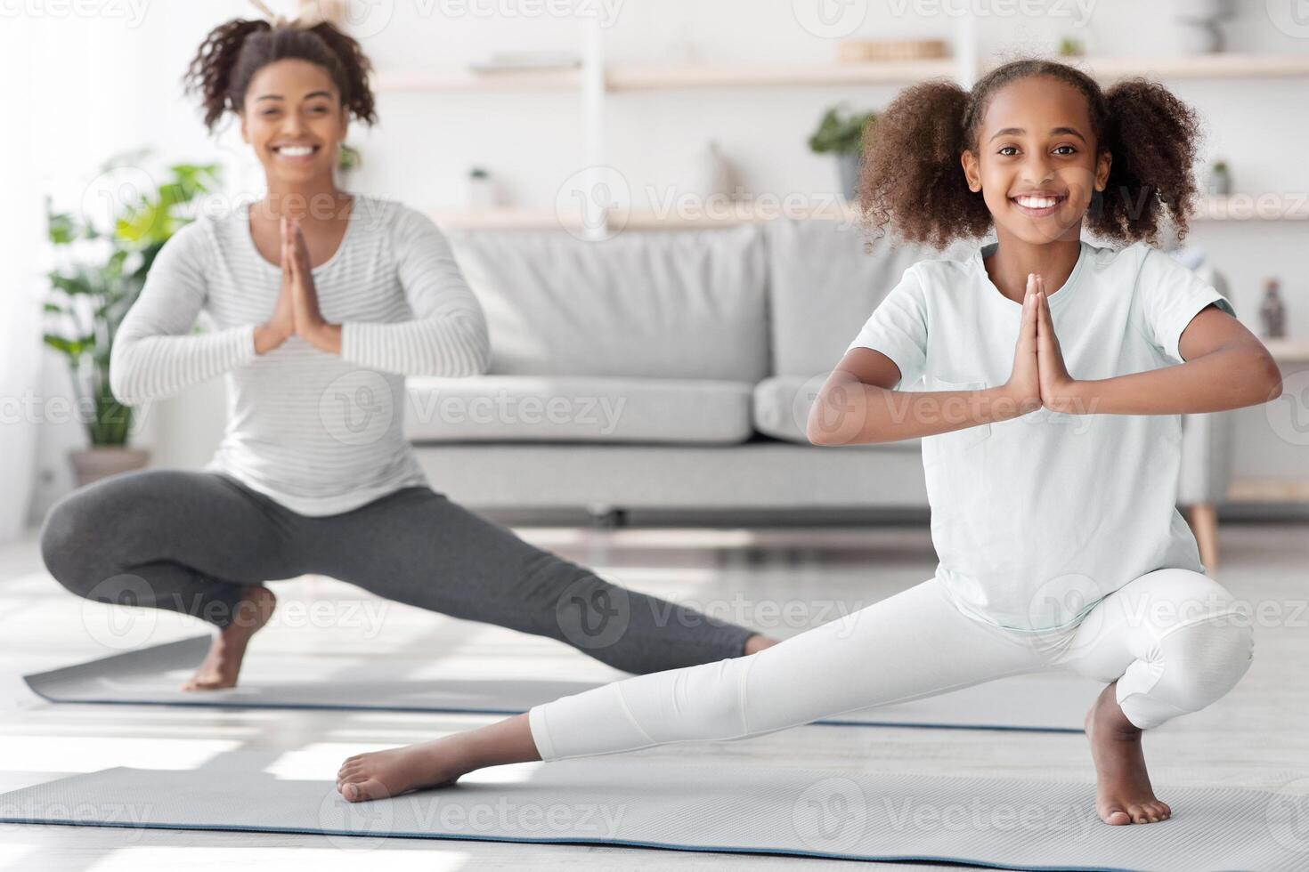 Sporty black family mother and daughter exercising at home, having yoga practise. Happy african american parent and girl kid in sportswear having moring training together in living room photo