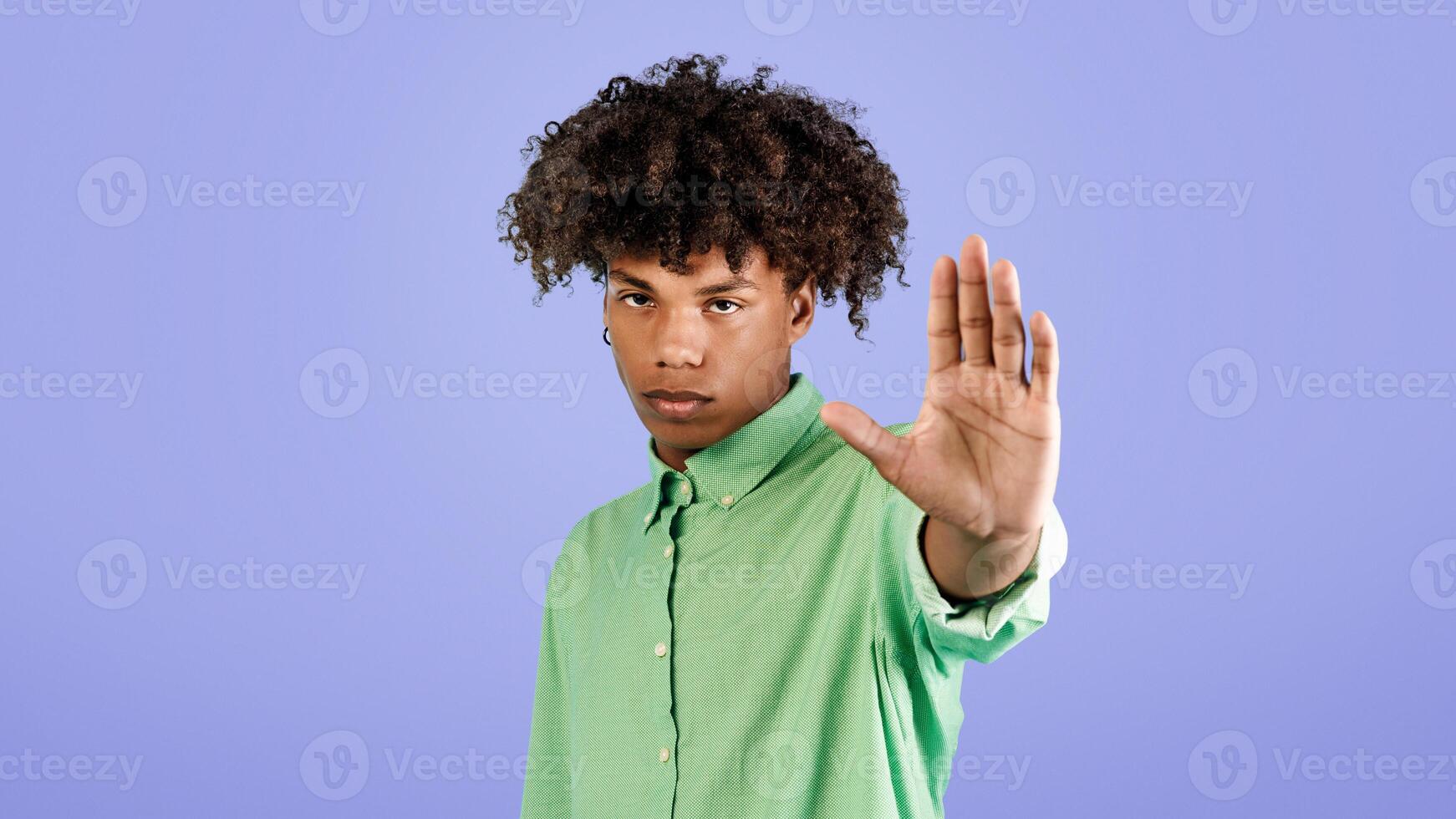 Serious black guy gesturing STOP, saying NO, showing rejection gesture, expressing refusal or denial, standing on blue studio background. Negative opinion concept photo