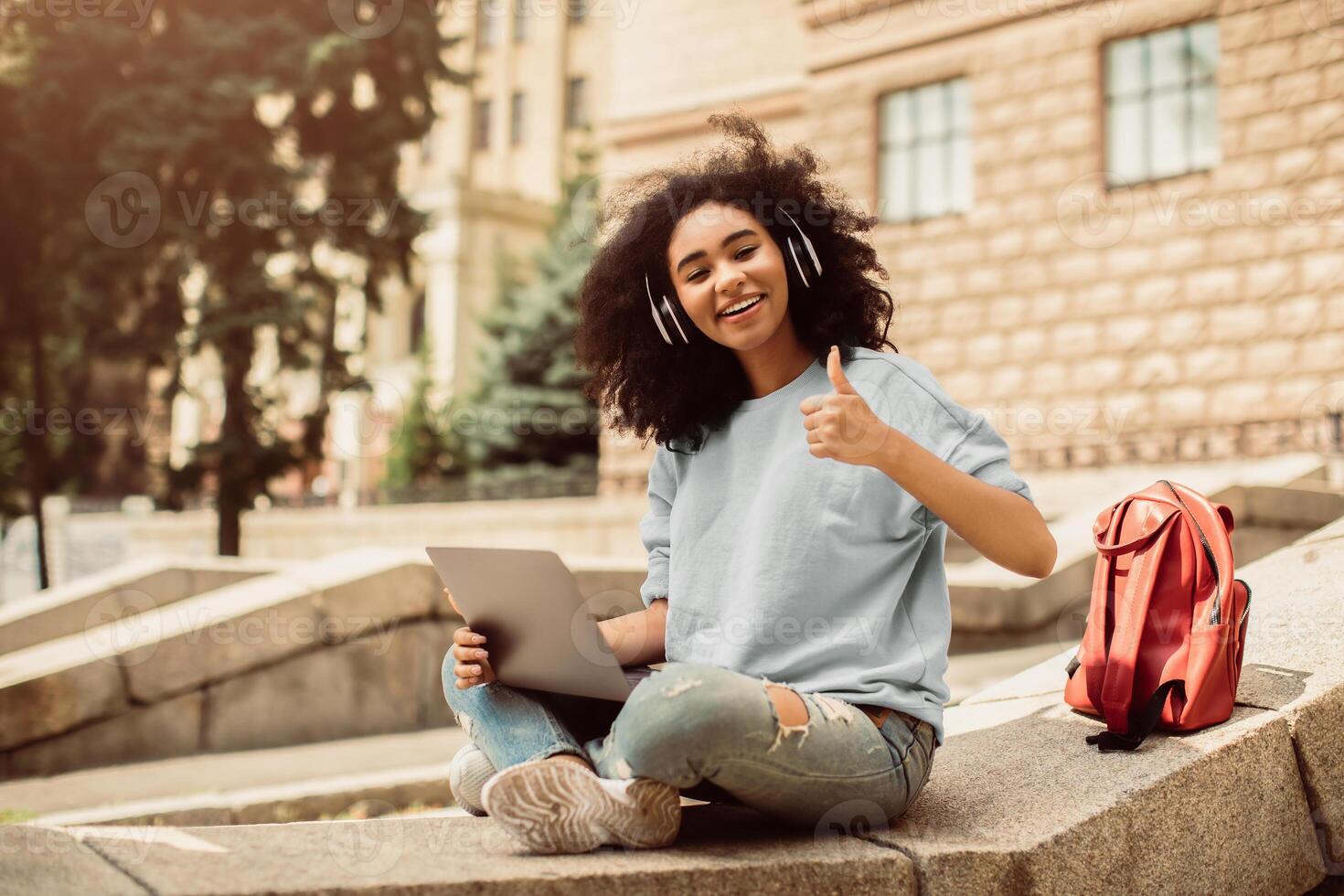 Black Teenager Girl Learning Online Using Laptop And Showing Like Gesture Smiling To Camera Approving E-Learning And Distance Study Sitting Outside. Student With Computer Gesturing Thumbs Up photo