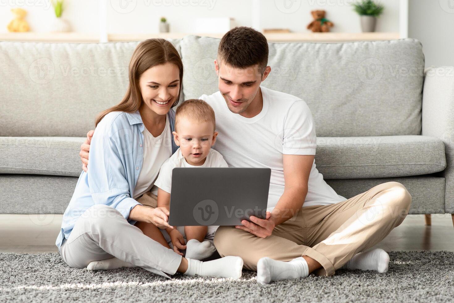 Happy Young Parents And Their Toddler Baby Using Laptop Together At Home While Relaxing On Floor In Living Room, Millennial Family Of Three Shopping Online Or Browsing Internet On Computer photo