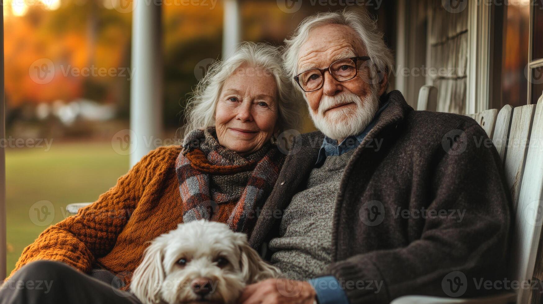 A couple in their golden years relaxes on a cozy porch with their dog during a sunny autumn afternoon, surrounded by vibrant leaves and a peaceful landscape. photo