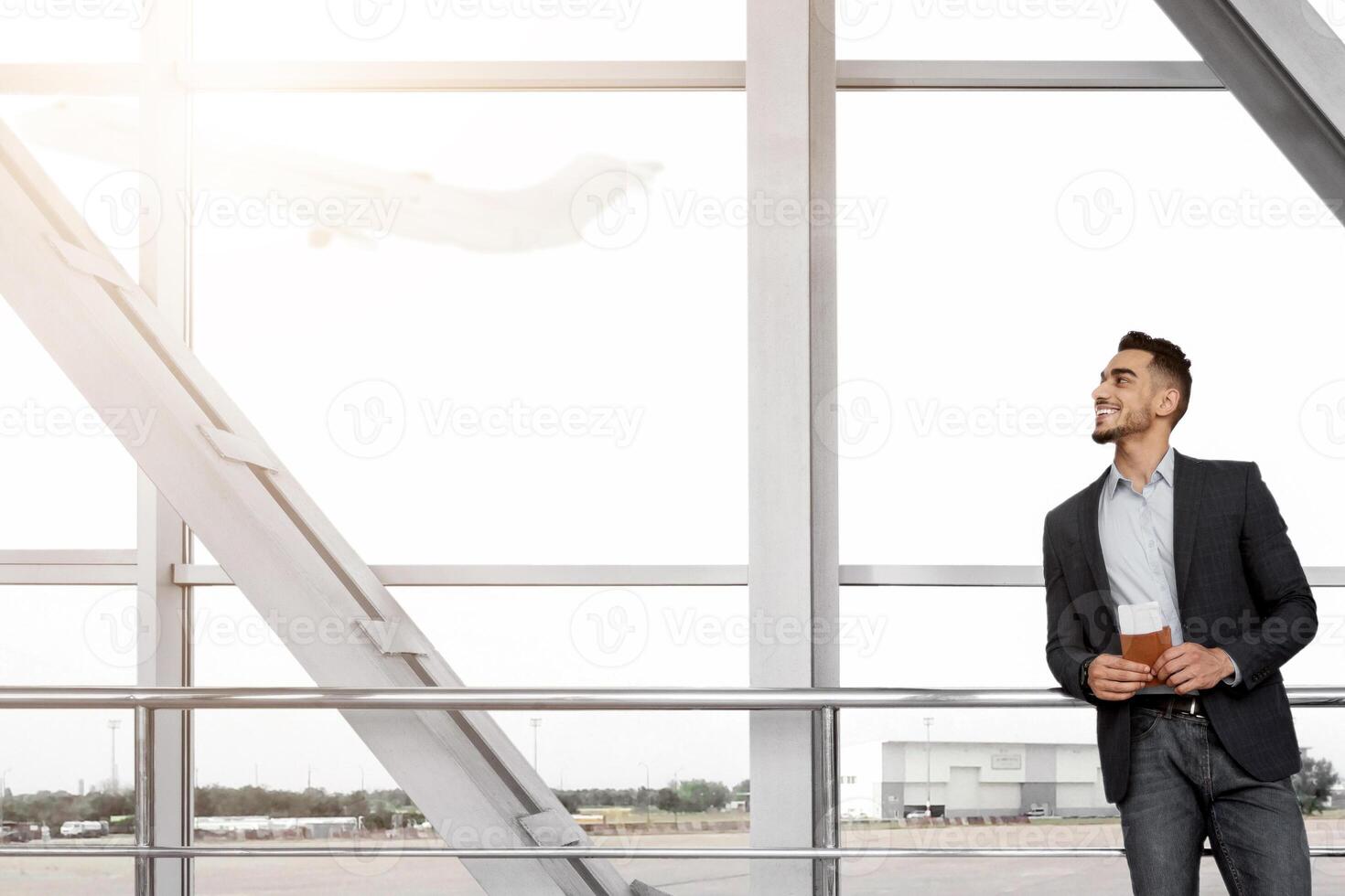Handsome Arab Man Holding Passports And Tickets Standing With Suitcase Near Window In Airport Terminal, Young Middle Eastern Entrepreneur Waiting For Boarding, Enjoying Business Trip, Copy Space photo