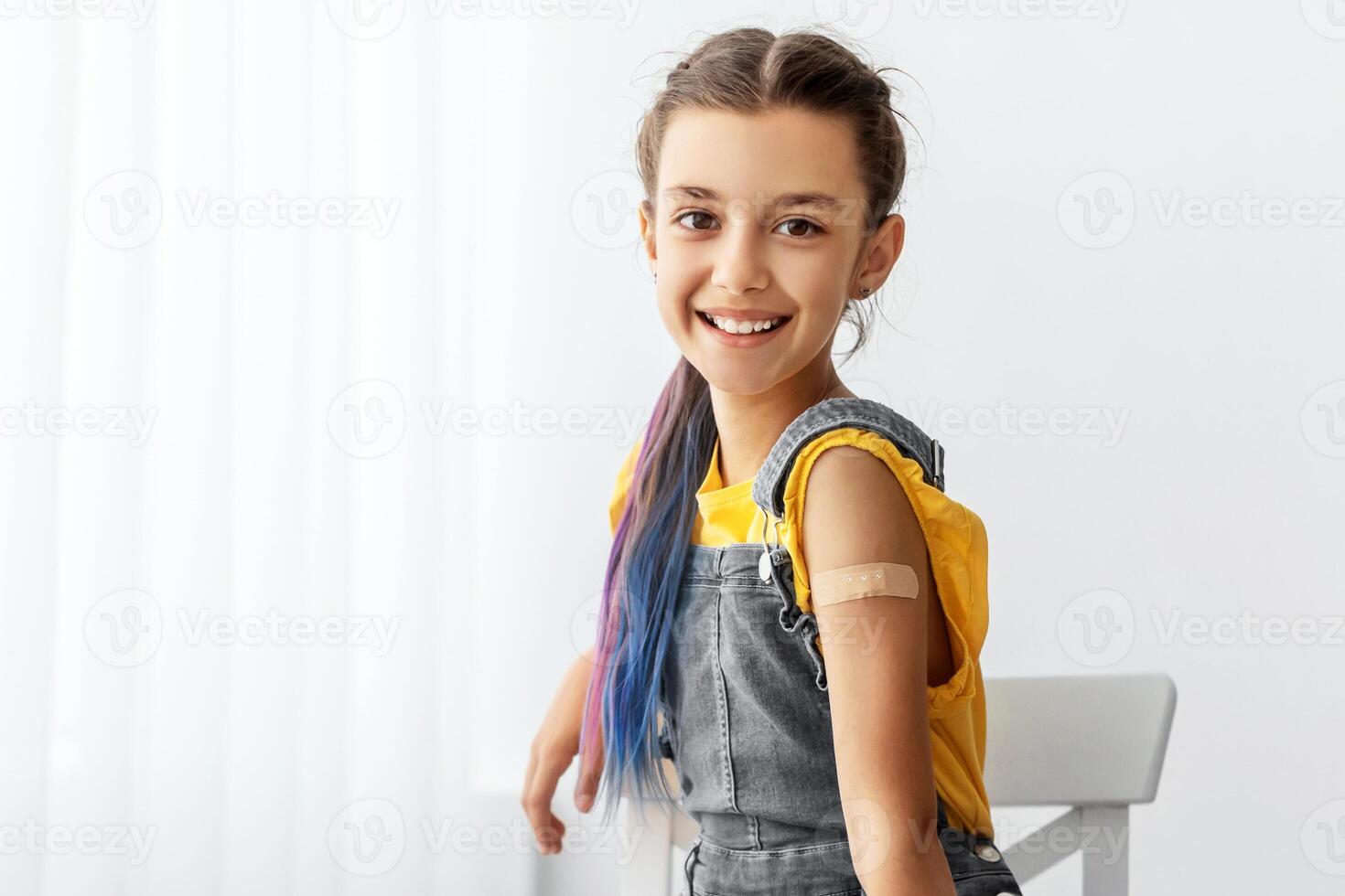 Vaccination, Protection. Happy Adolescent Girl Showing Vaccinated Arm With Adhesive Bandage Plaster On Shoulder After Getting Corona Virus Covid Vaccine In Clinic Sitting On Chair. Antiviral Injection photo