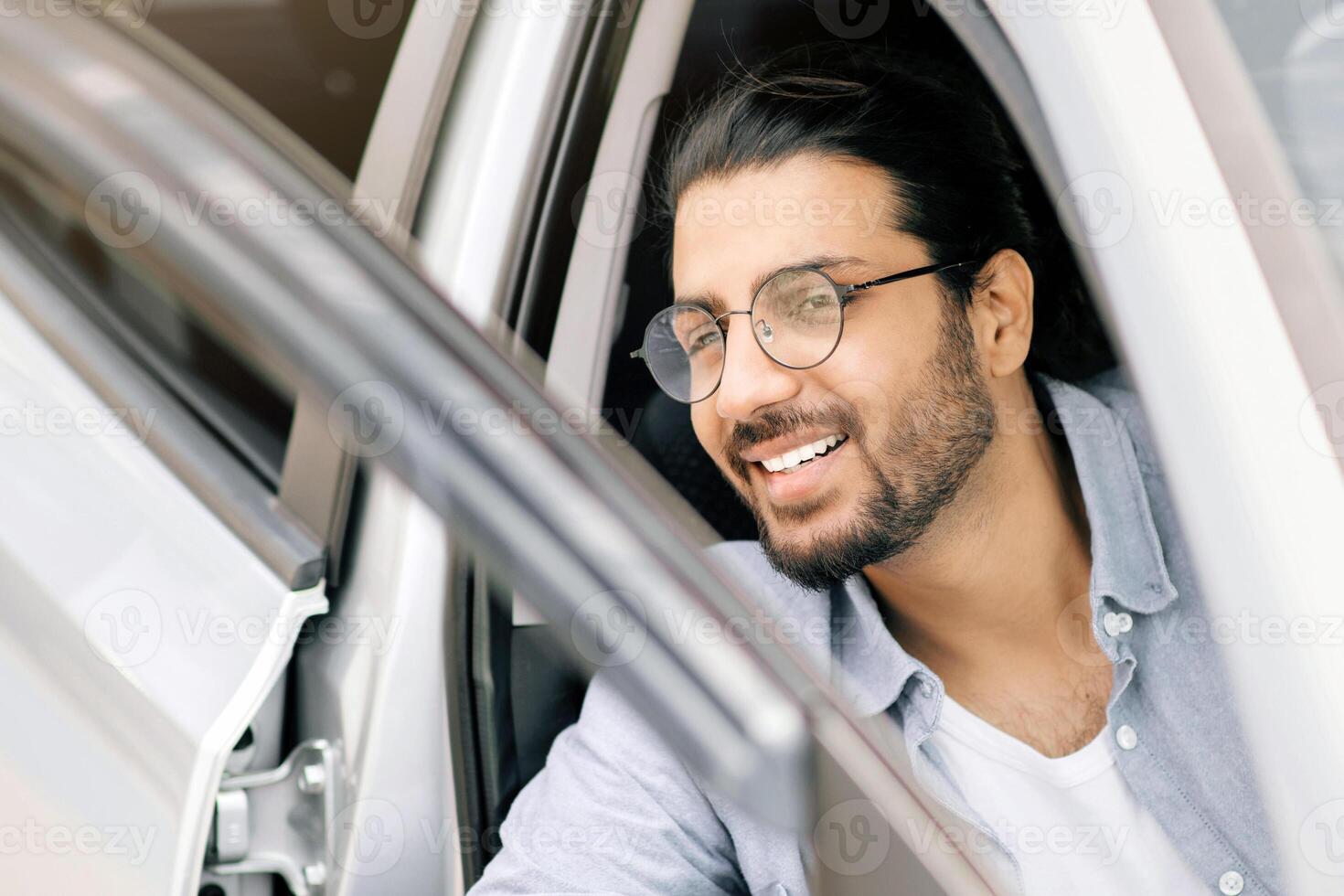 Successful young middle-eastern man going out the car, closeup photo. Happy arab guy open automobile door and smiling, getting in. Auto test-drive, leasing, buying, renting concept photo