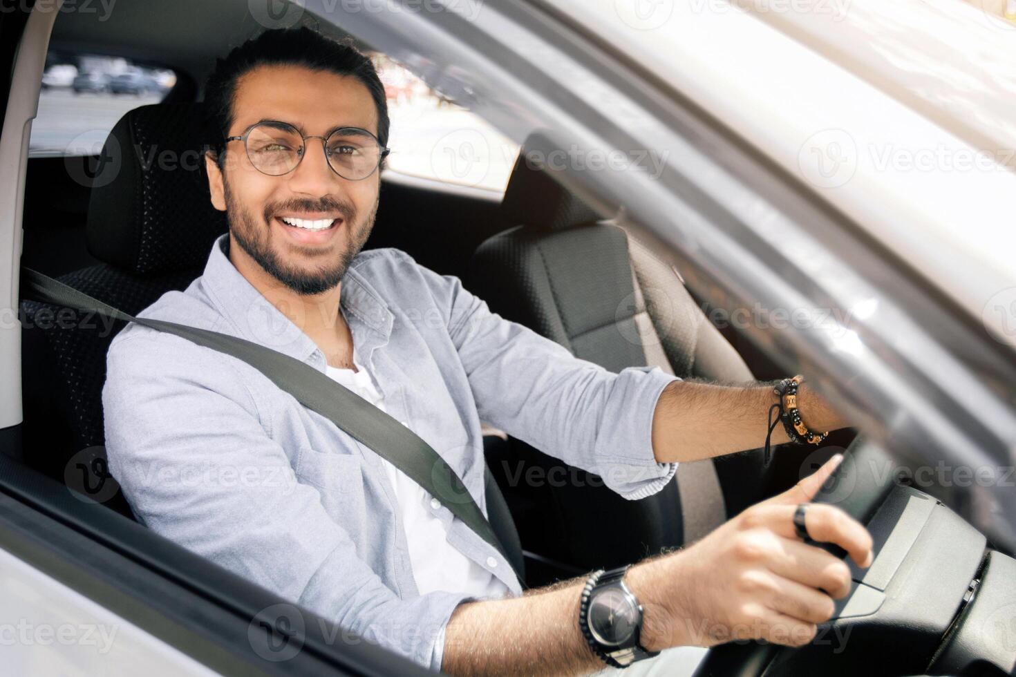 Handsome stylish middle-eastern man driving nice auto, looking through car window and smiling at camera, going to office or travelling alone by automobile, closeup photo, copy space photo