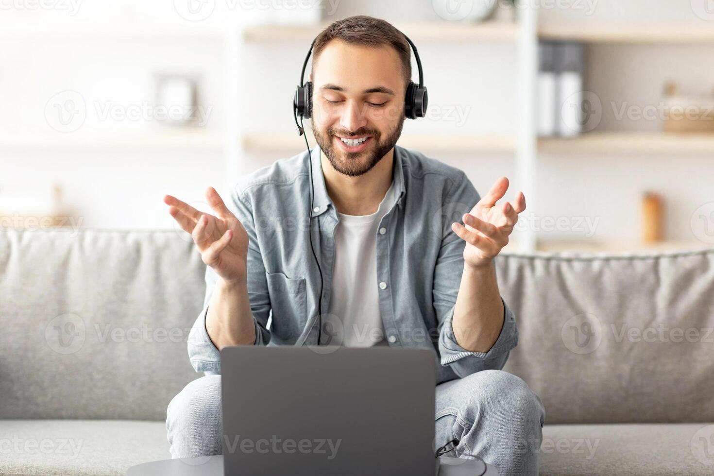 Happy young guy in headset making call on laptop at home, talking to camera. Young Caucasian man enjoying online communication, participating in web conference or business meeting photo