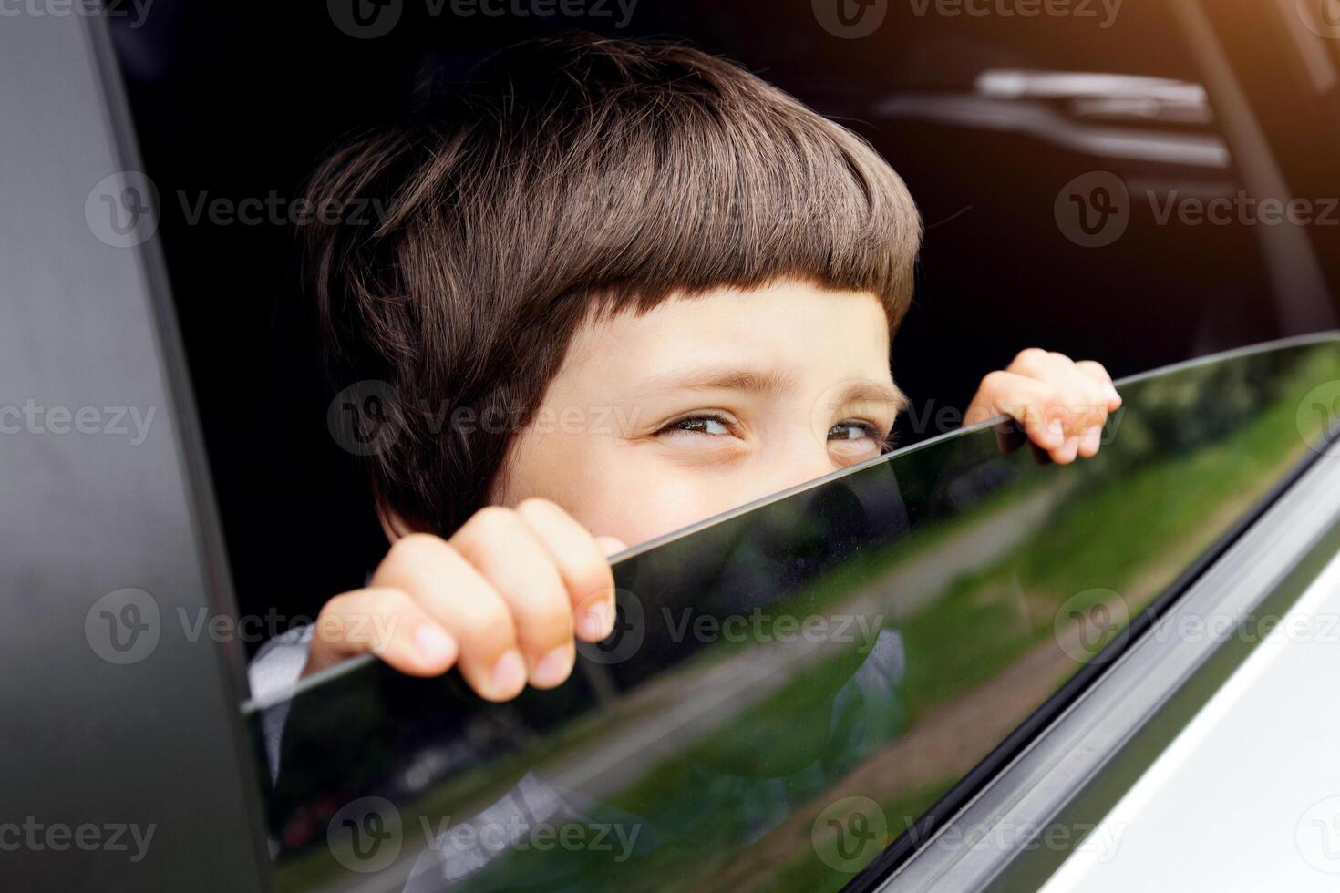 Curious Little Boy Peeking Out Of Open Car Window During Ride, Cheerful Cute Small Male Child Sitting On Back Seat Of Automobile And Looking Outside, Enjoying Road Drive Trip, Closeup Shot photo