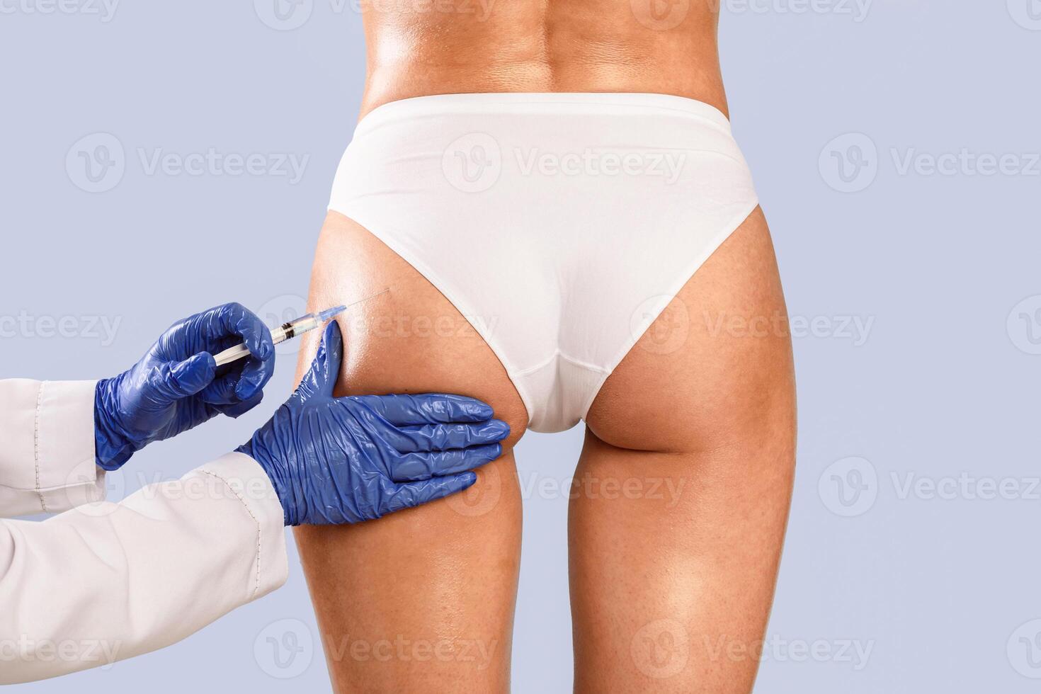 Butt Lifting Concept. Rear back view of slim woman having hip injection at beauty salon, closeup. Plastic surgeon making injection at buttocks area for unrecognizable lady, blue studio background photo