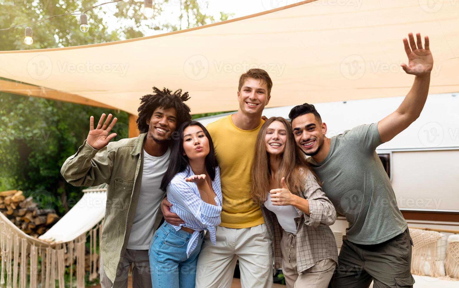 Portrait of happy young multiracial friends posing near their camper van, looking at camera and making different gestures, smiling and having fun together during summer vacation photo