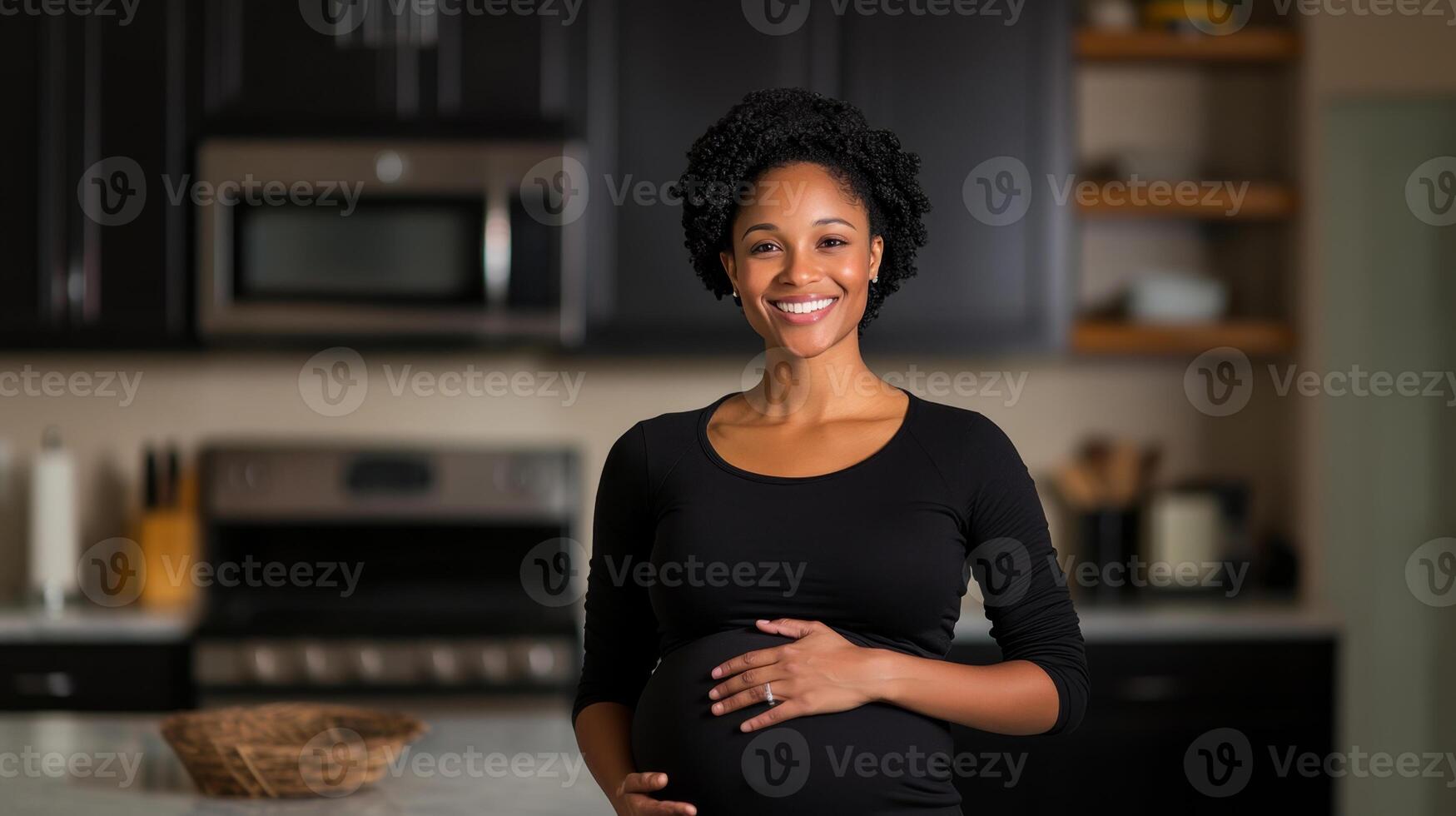 A smiling woman stands in a kitchen, cradling her baby bump. The modern space is warmly lit, reflecting a serene atmosphere. She enjoys this beautiful phase of her life with happiness. photo