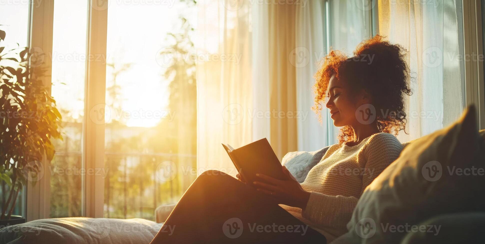 A woman rests comfortably on a couch in her home, reading a book. Sunlight filters through the curtains, creating a cozy atmosphere. Her pregnancy adds to the warmth of this peaceful moment. photo