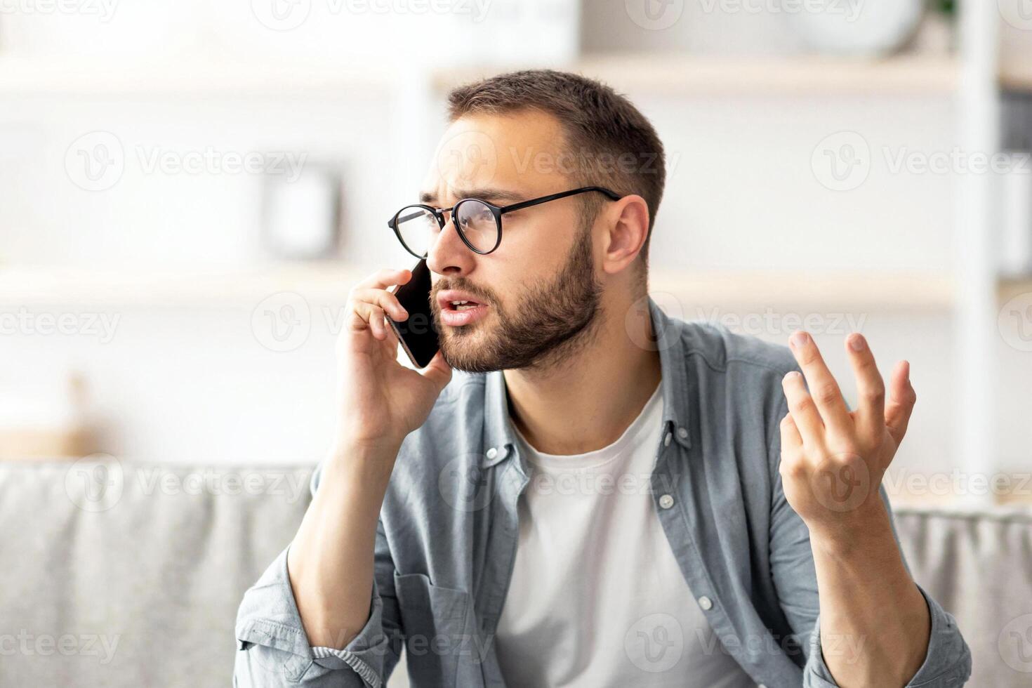 Stressed young freelancer using laptop and making call on smartphone at home office. Millennial Caucasian man overworking to meet deadline, having error in his project photo