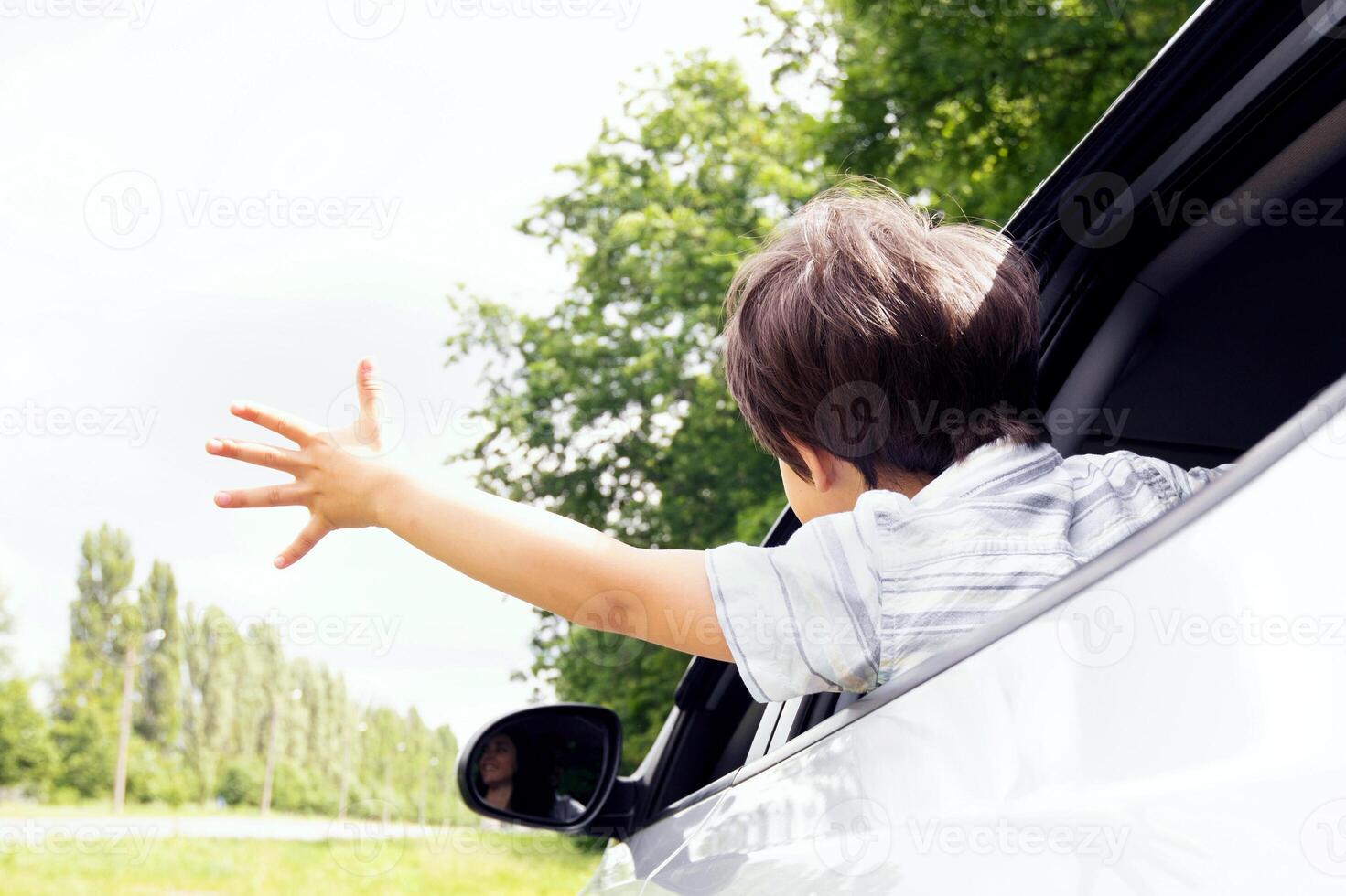Rear view of little boy leaning out of car window and trying to catch wind with outstretched hand, small male child enjoying summer weather and automobile ride, on the move shot, closeup photo