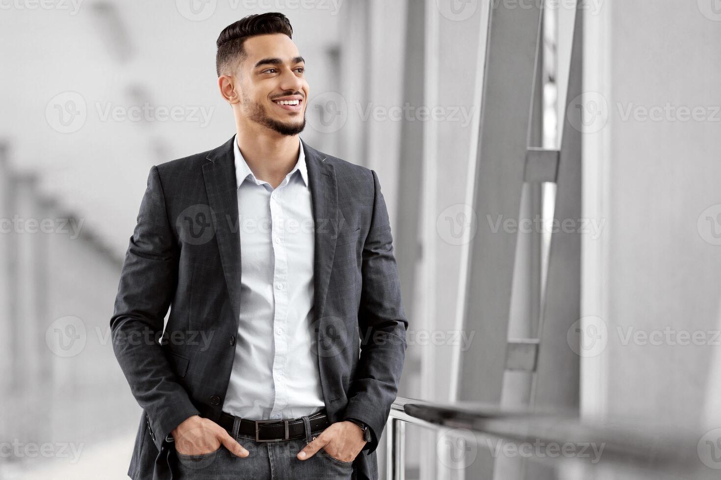 Handsome Young Middle Eastern Man Waiting Flight At Airport Terminal, Smiling Millennial Arab Businessman Standing With Hands In Pockets And Looking At Window, Ready For Trip, Copy Space photo