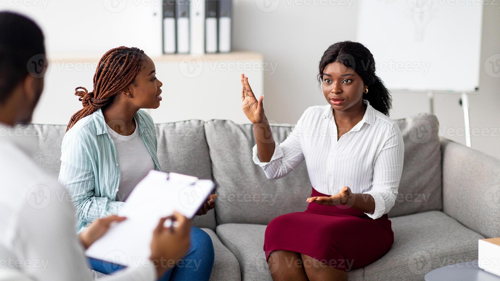 African American lesbian couple having consultation with psychologist at office. Young LGBT homosexual family receiving professional help with their relationship problems photo