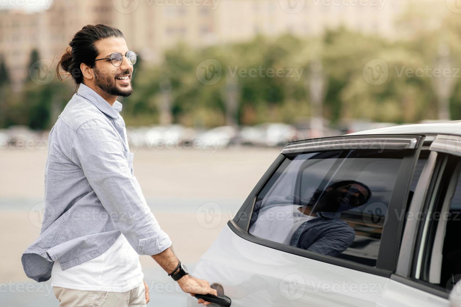 Cheerful middle-eastern young man in casual getting in taxi, open auto back door, taking cab home or to business meeting, looking at copy space. Car service, transportation, taxi concept photo
