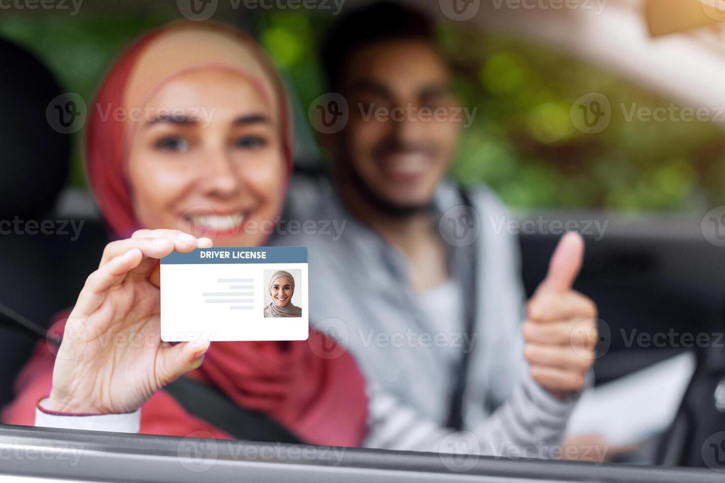 Glad middle eastern male and female in hijab show driving license and thumb up in open window in car after exam, outdoor in summer. Get license, driving test, lesson with teacher and life insurance photo