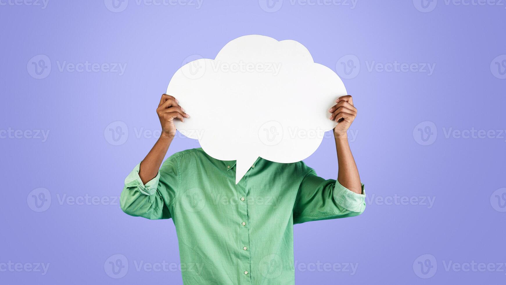 Unrecognizable african american young guy holding an empty speech bubble in front of his head, posing over blue studio background, free copy space photo