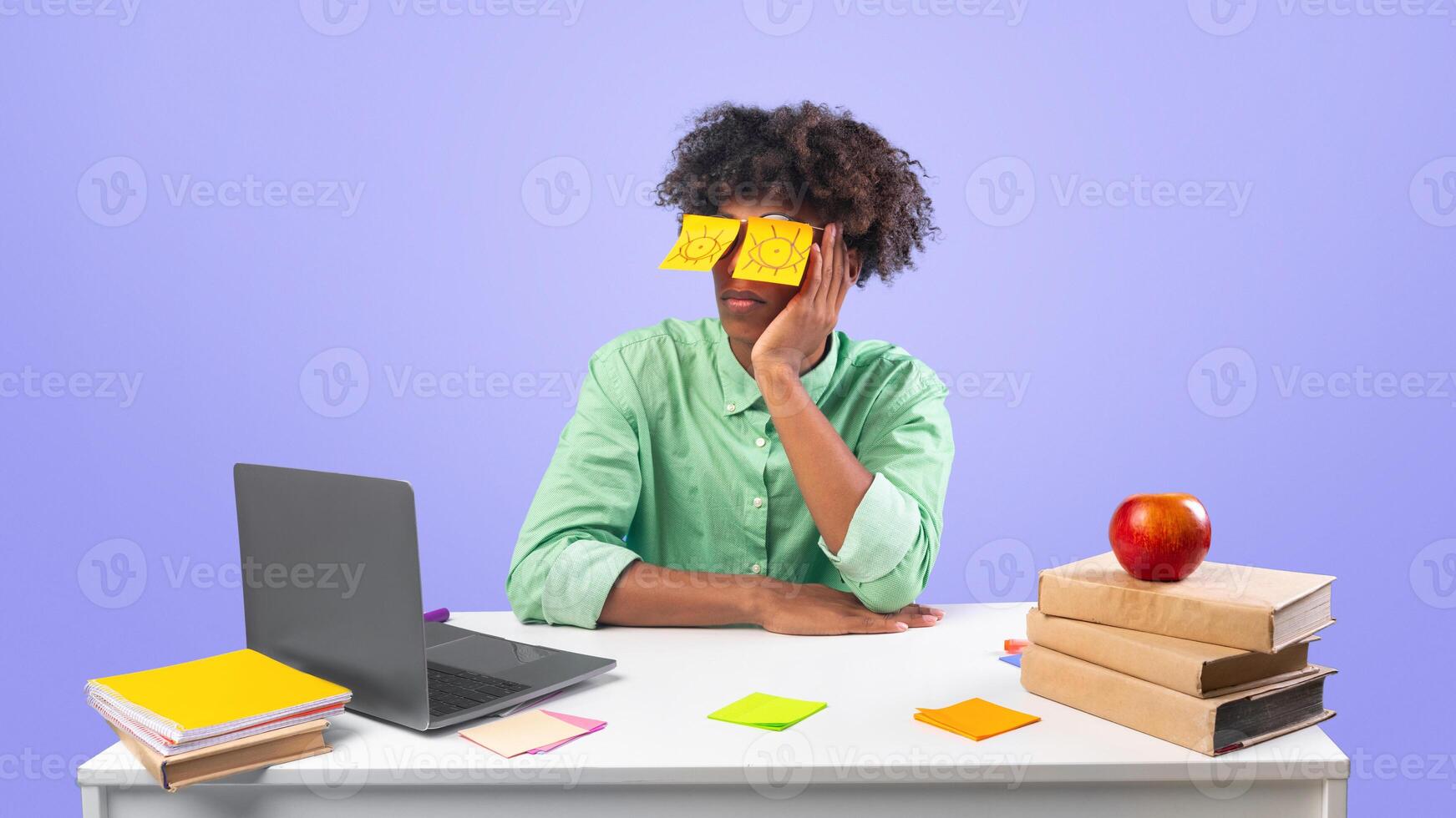 Exhausted student. Black teen guy with painted eyes on stickers sitting at desk and sleeping in front of laptop, unproductive lazy teenager dozing, working on difficult project over blue background photo