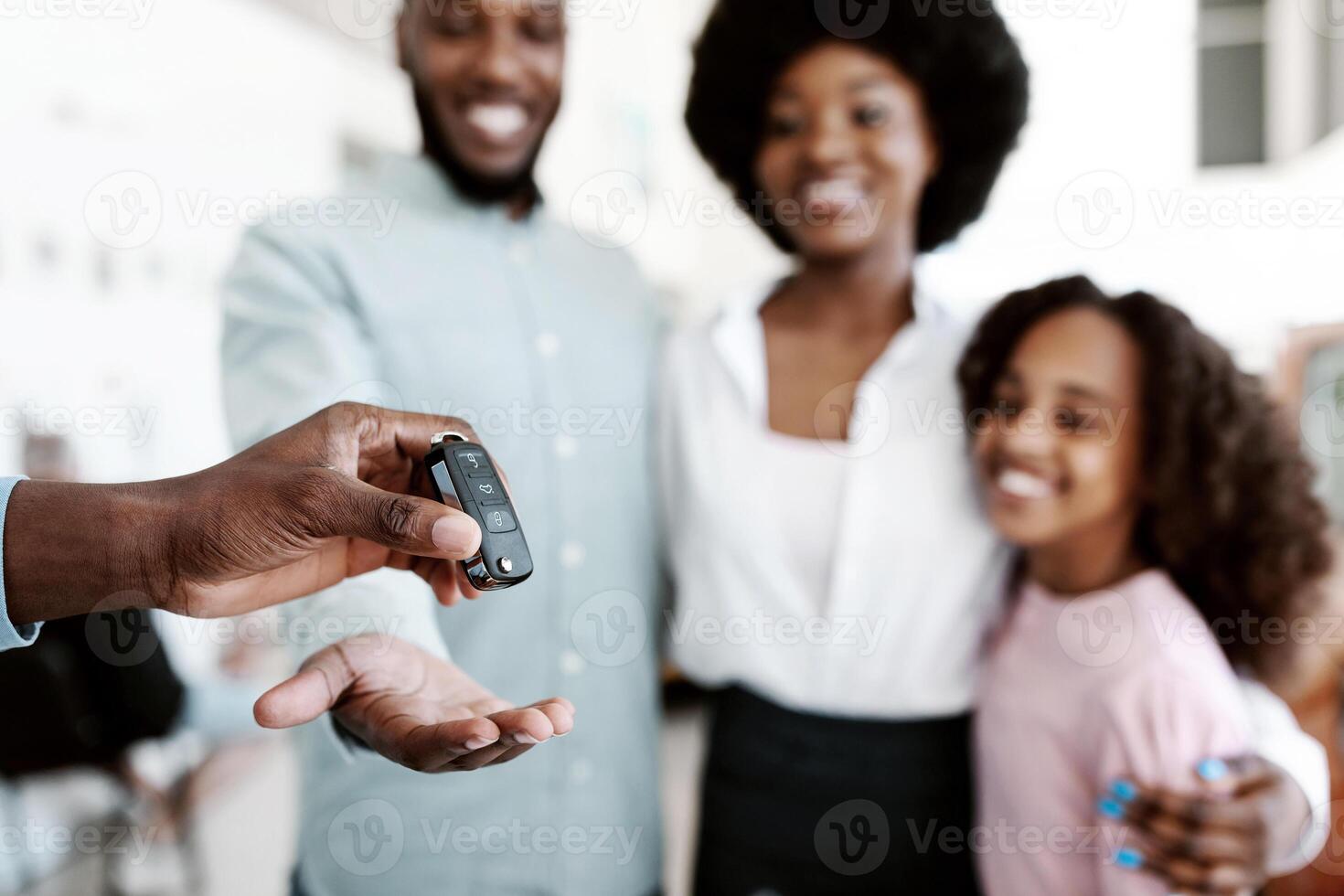 Manager giving new car key to young black family at auto dealership store, selective focus. Happy African American customers buying vehicle from salesman at automobile showroom photo