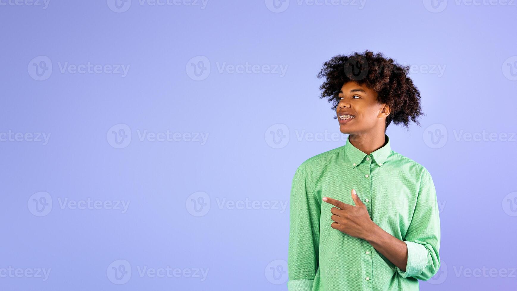 Look at this. Excited african american student guy pointing and looking aside at empty space, standing over blue background, studio shot, copy space. Cool offer concept photo