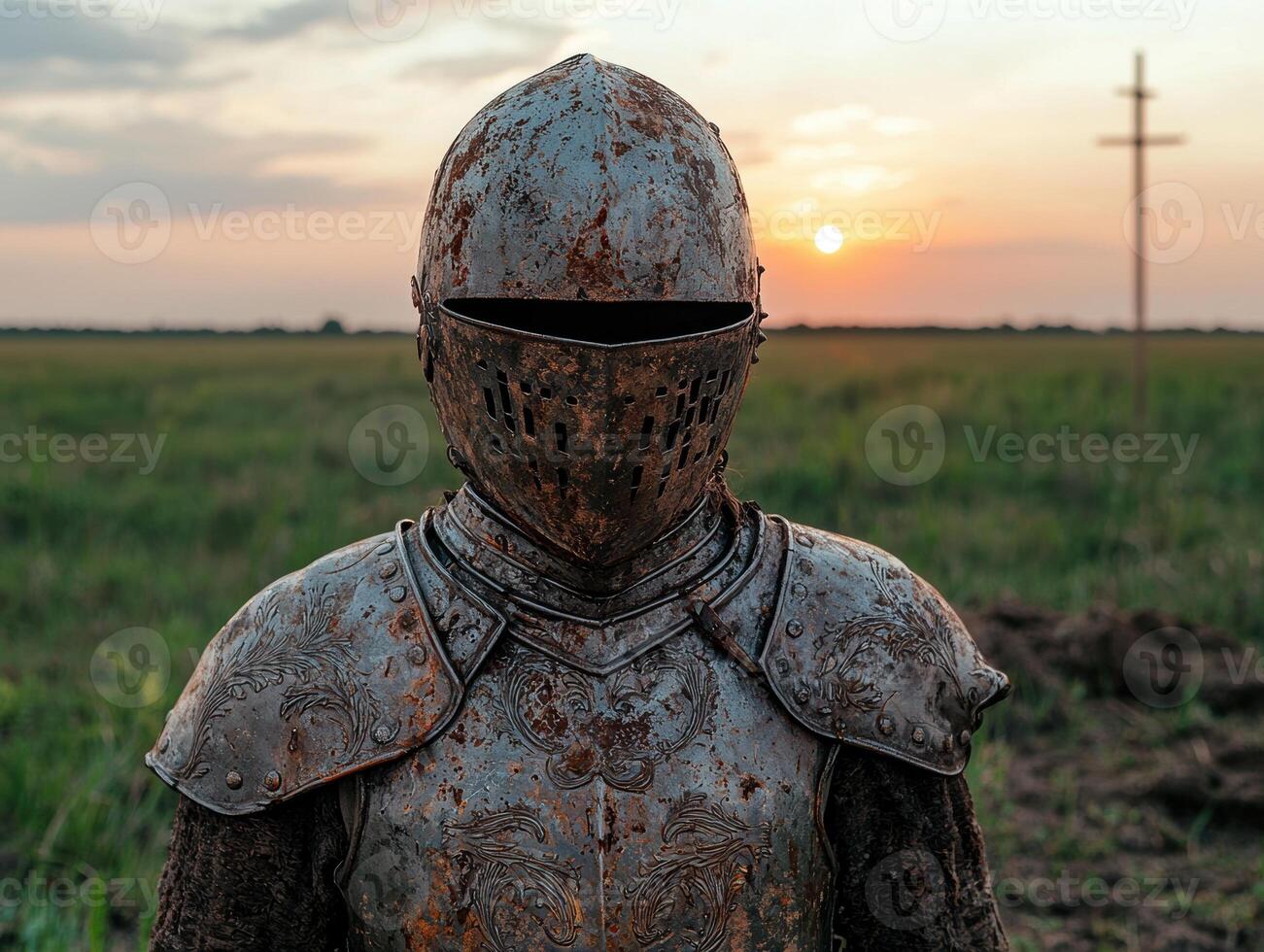 Medieval knight in rusty armor stands in a field at sunset photo