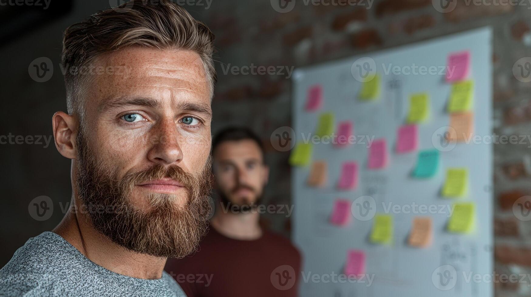 Confident businessman with beard looking at camera, colleague in background, brainstorming session photo